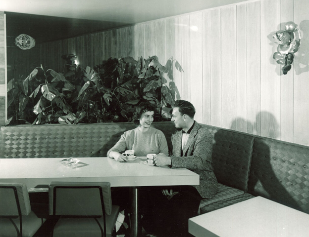 Prompt B. A couple students stare into each others eyes as they sit together in a booth while holding mugs.